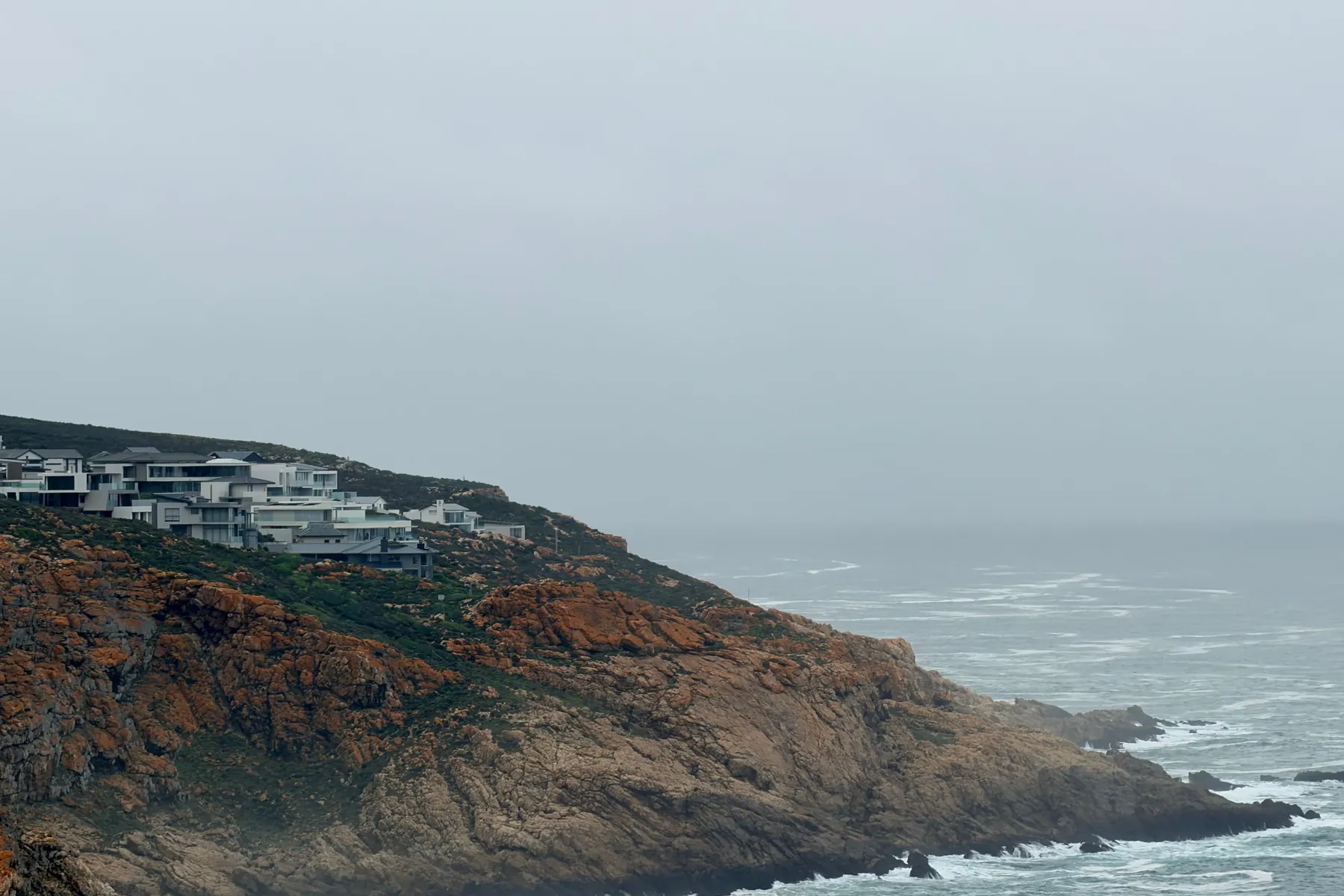 Modern houses on rocky cliffs above a misty ocean