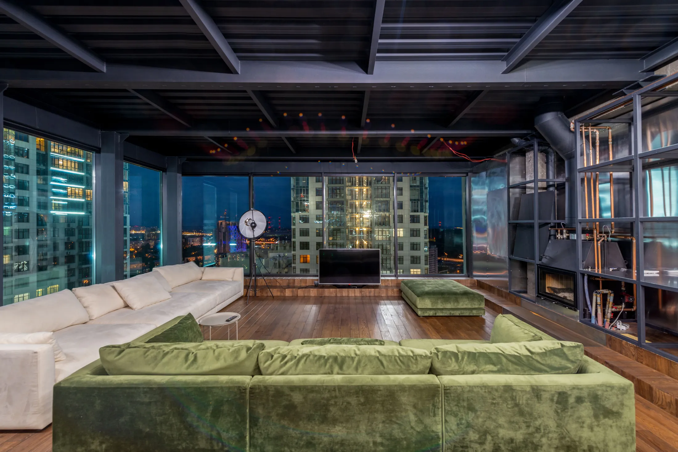 The double-height living level of the Works penthouse at dusk, city lights beyond